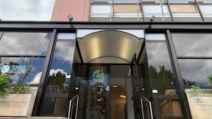 L’entrée d’un hôtel avec une façade en verre, un logo bien visible et le reflet du ciel.