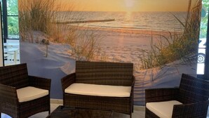Une pièce meublée de mobilier en osier, avec une table en verre et une fresque murale représentant une plage.