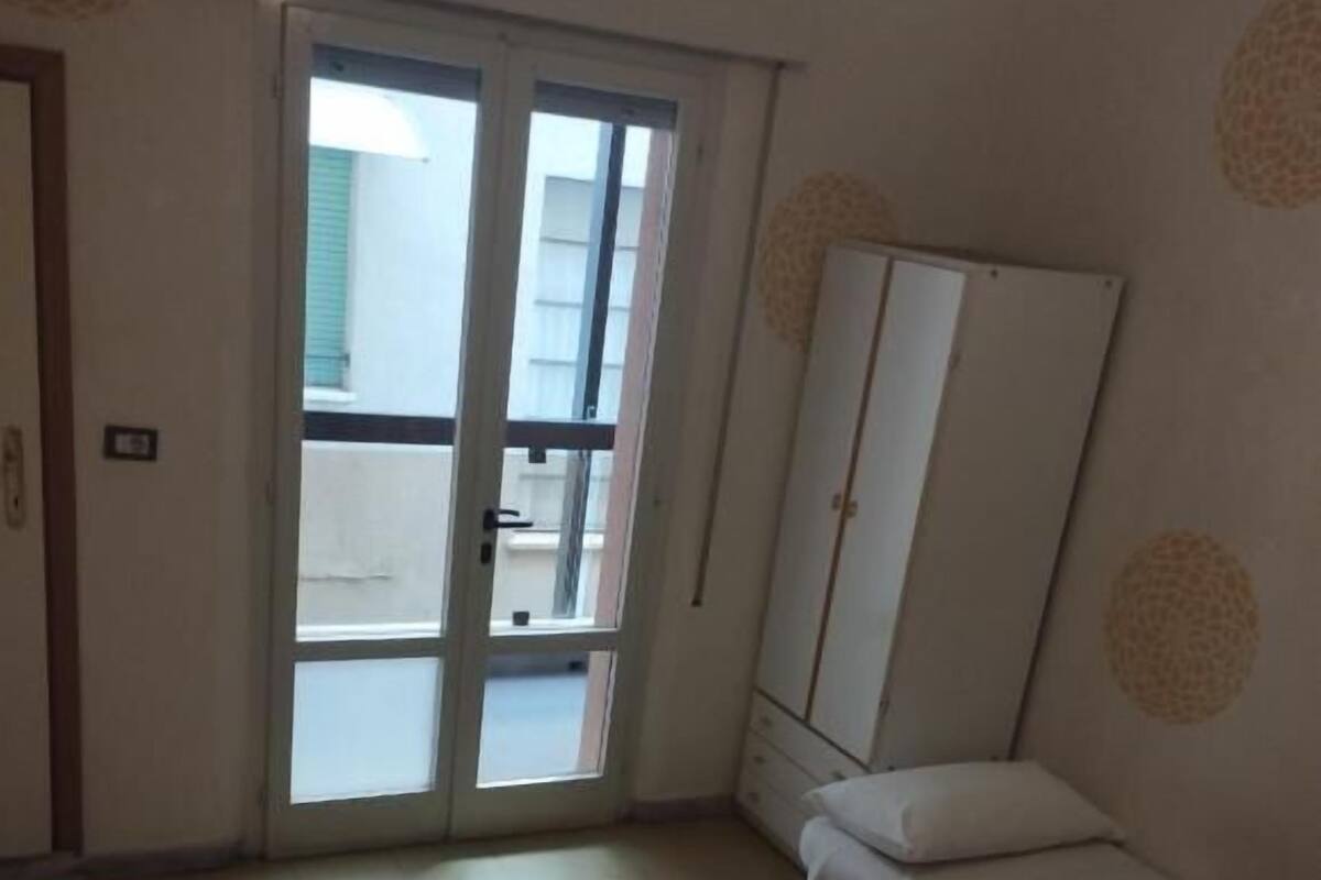 Quarto de hotel com cama, uma pequena mesa, guarda-roupa e uma porta de vidro deslizante para área externa.