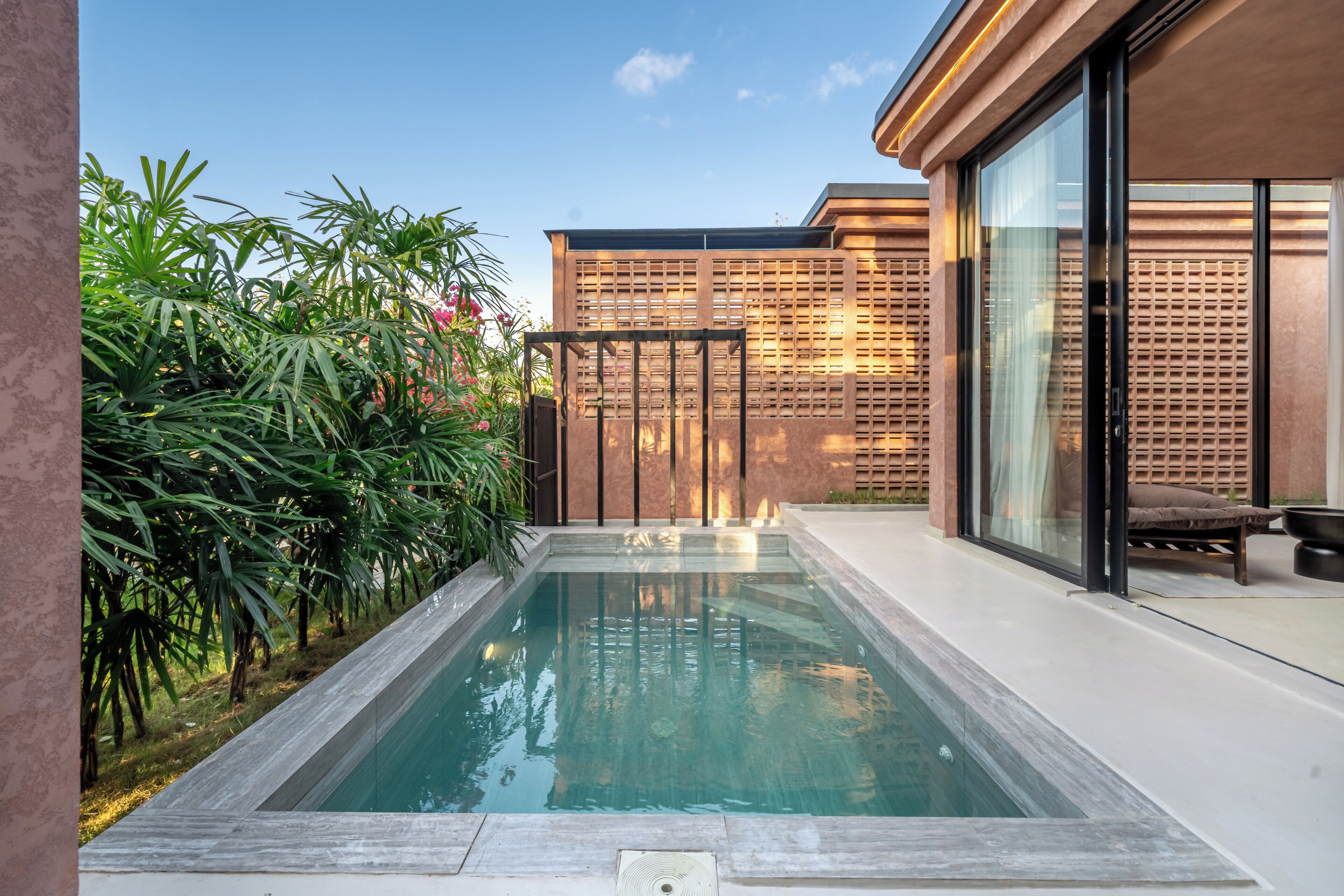 Una piscina con muelle de madera, rodeada de exuberante vegetación y un edificio moderno con grandes ventanales.