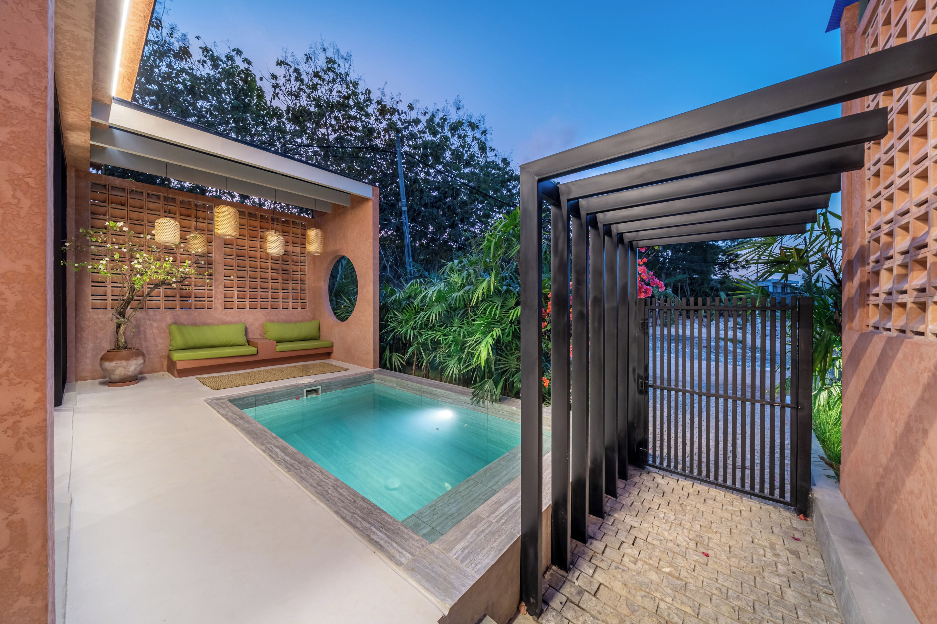 Un espace piscine extérieur moderne, agrémenté d’un canapé vert, d’une plante en pot et d’une structure en forme de pergola.