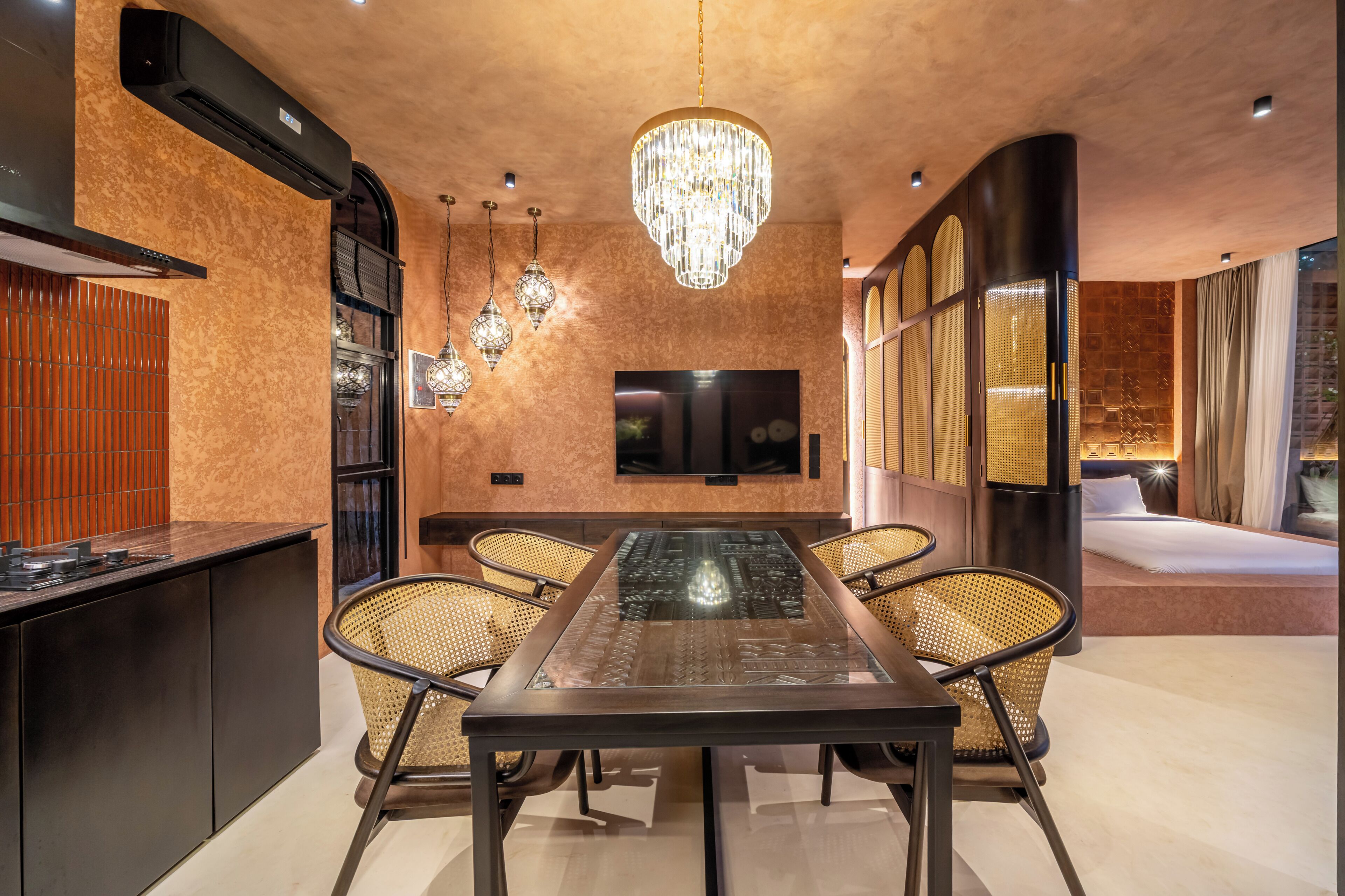 A modern hotel room with a dining area, a large chandelier, a flat-screen TV, and a bed with a canopy.