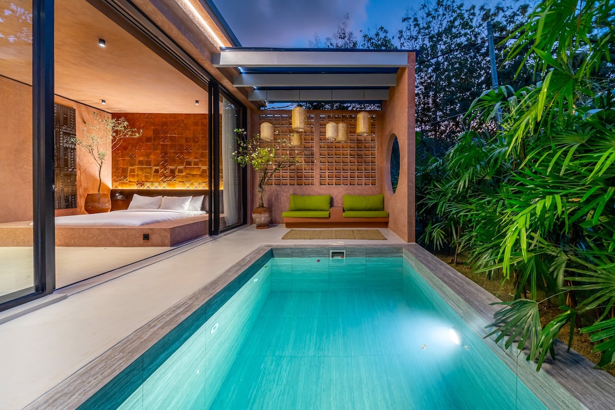 Un área de piscina exterior moderna con cerramiento de vidrio, un espacio de descanso con cojines y un muro de madera con diseño de cuadrícula.