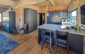 A modern kitchen with a central island, bar stools, and a view through the window.