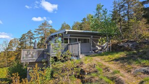 Eine Hütte mit einer Terrasse, umgeben von Bäumen und blauem Himmel.