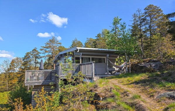 A cabin with a deck, surrounded by trees and a clear sky.