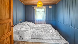 Ein Zimmer mit Bett, Holzwänden, einem Fenster mit durchsichtigen Vorhängen und einer Hängelampe.