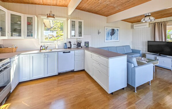 A modern kitchen with white cabinetry, a built-in oven, and a dining area with a blue sofa and a flat-screen TV.