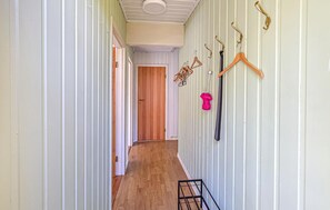 A hallway with wooden flooring, a door at the end, and a rack with hangers and a pink item.