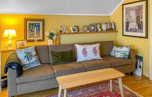 Un salon avec un canapé, une table basse, une lampe, des tableaux encadrés et une peinture au mur.