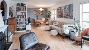 Una sala de estar con chimenea, un sofá, una mesa de comedor con sillas, una estantería y un ventanal grande.