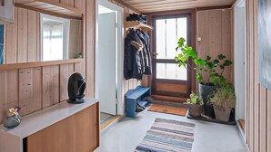 Interior de madera con un banco, perchero, planta en maceta y una puerta.