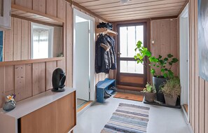 Un intérieur en bois avec un banc, un porte-manteau, une plante en pot et une porte.