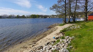 Vista de un lago con playa arenosa, rocas y árboles.