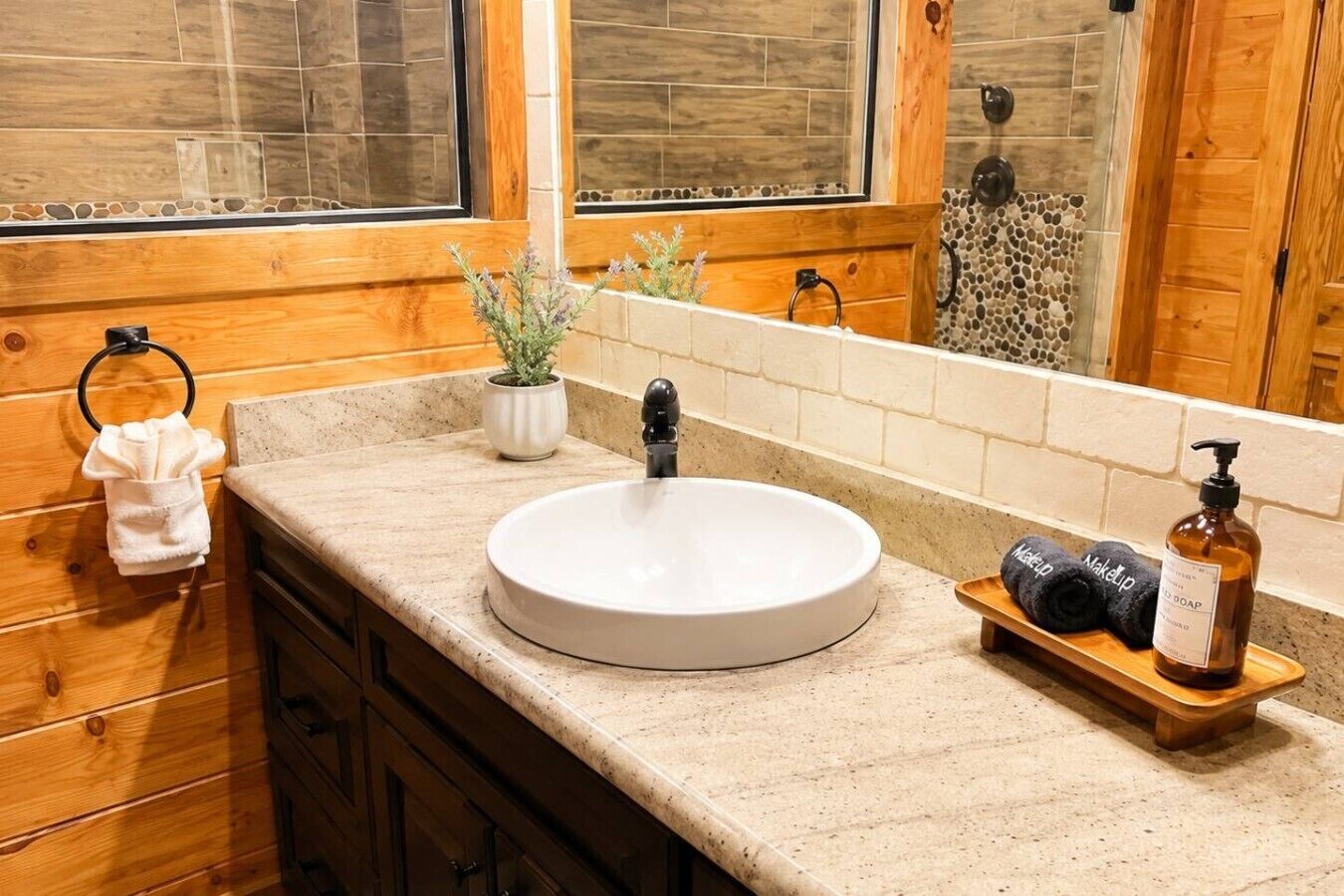 Une salle de bain avec un lavabo rond, des meubles en bois, un porte-serviettes, une petite plante en pot et un distributeur de savon.