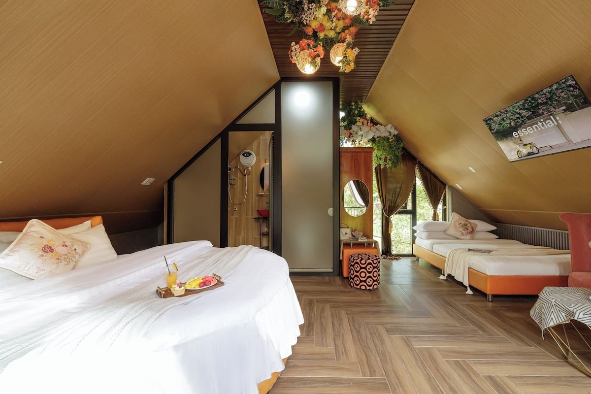 A bedroom with a sloped ceiling, a bed with a tray of fruit, and a small table with a chair.