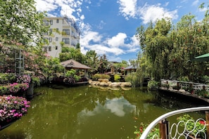A tranquil garden with a pond, a bridge, and a building with balconies. - Up Tree Garden Da Lat (Da Lat)