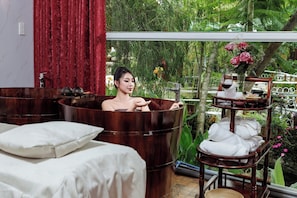 A spa room with a large wooden tub, a wooden shelf with towels, and a view of greenery outside. - Up Tree Garden Da Lat (Da Lat)
