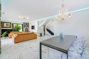 Ein modernes Wohnzimmer mit einer Couch, einem Esstisch mit Stühlen, einer Deckenleuchte und einer Treppe.