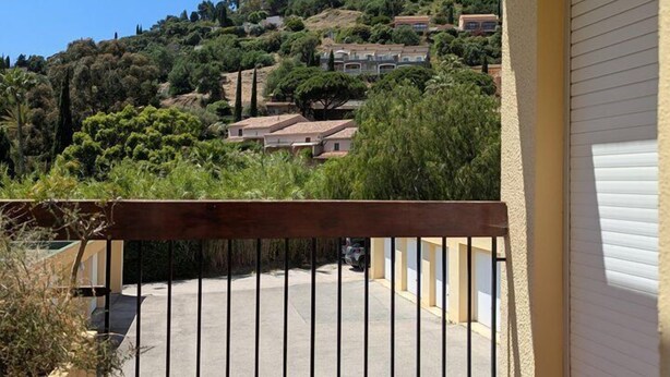 Ein Balkon mit Metallgeländer, einem Blumentopf und Blick auf eine Hügelkuppe mit Gebäuden.