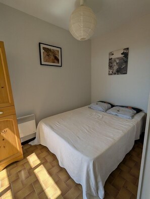Ein Schlafzimmer mit einem Bett, einem Holzschrank, einem Heizkörper und zwei Bildern an der Wand.