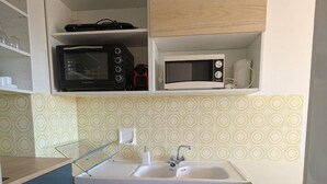 Eine kompakte Küche mit Spüle, zwei Mikrowellen und einer Pendelleuchte.