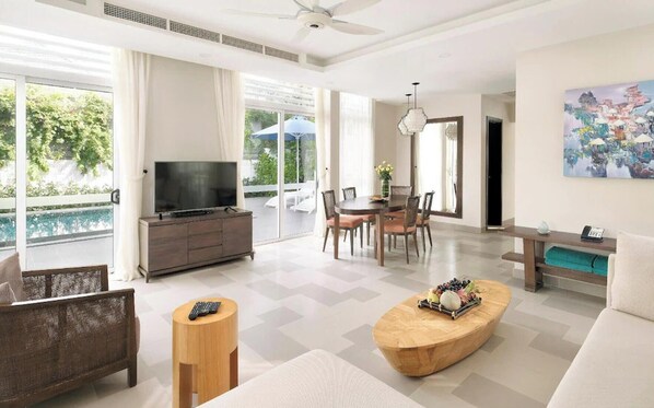 A spacious living room with a TV, dining area, and a balcony with a pool view.