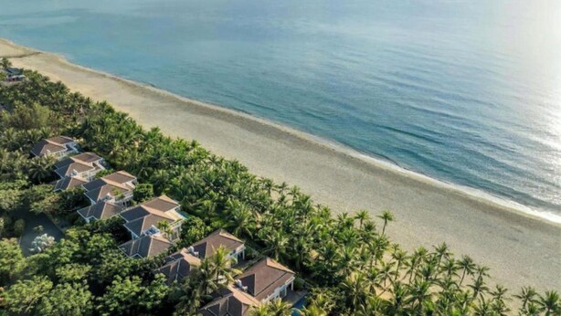 Un complejo turístico frente al mar con villas, palmeras y vistas al océano.