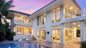 Una casa moderna de varios pisos, con piscina, balcones y un espacio al aire libre cubierto.