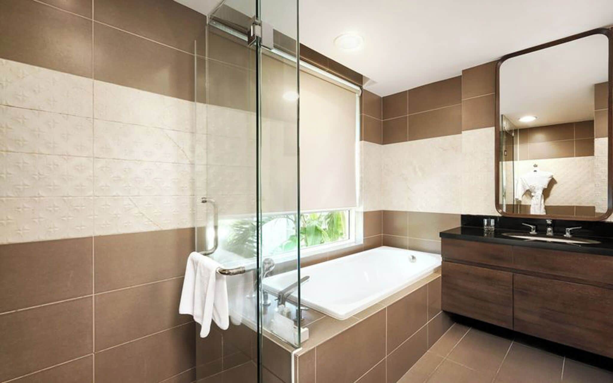A modern bathroom with a glass shower enclosure, a large bathtub, and a dark wooden vanity with a mirror.
