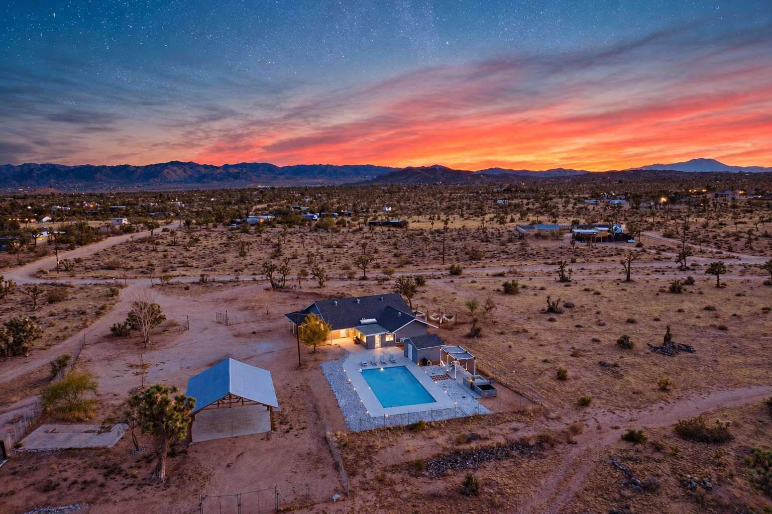 A desert landscape with a house featuring a swimming pool, a covered patio, and a small guest house.