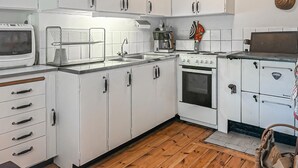 Une cuisine avec des meubles blancs, une cuisinière, un four à micro-ondes et un évier.