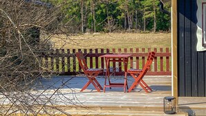 Une terrasse en bois avec une table et des chaises, une poubelle en métal et une clôture en bois.