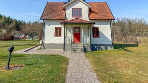Une maison à deux étages avec une porte rouge, des murs blancs et un toit recouvert de tuiles.