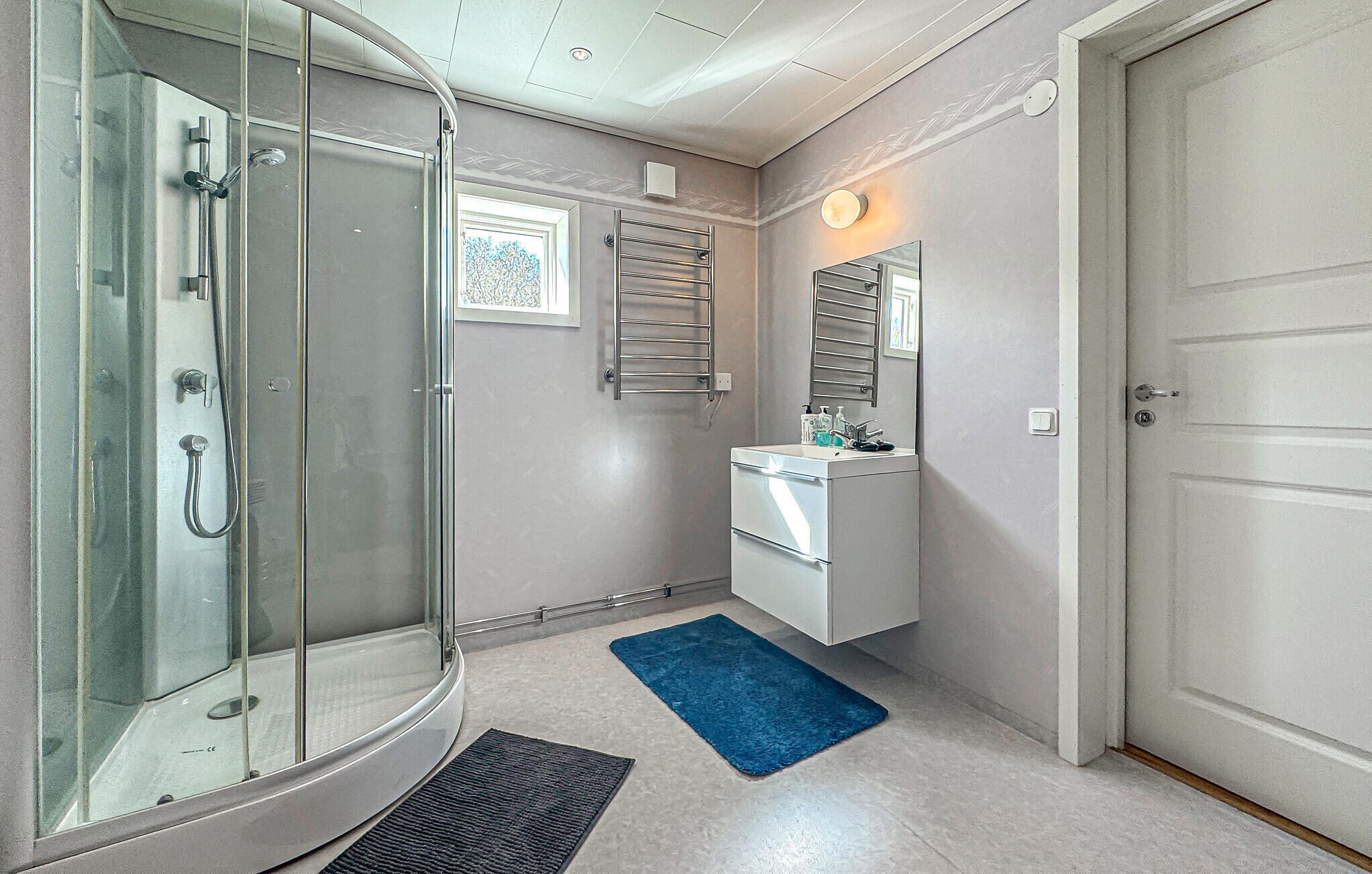 Un bagno con box doccia in vetro, un lavabo con specchio e un tappeto blu sul pavimento.