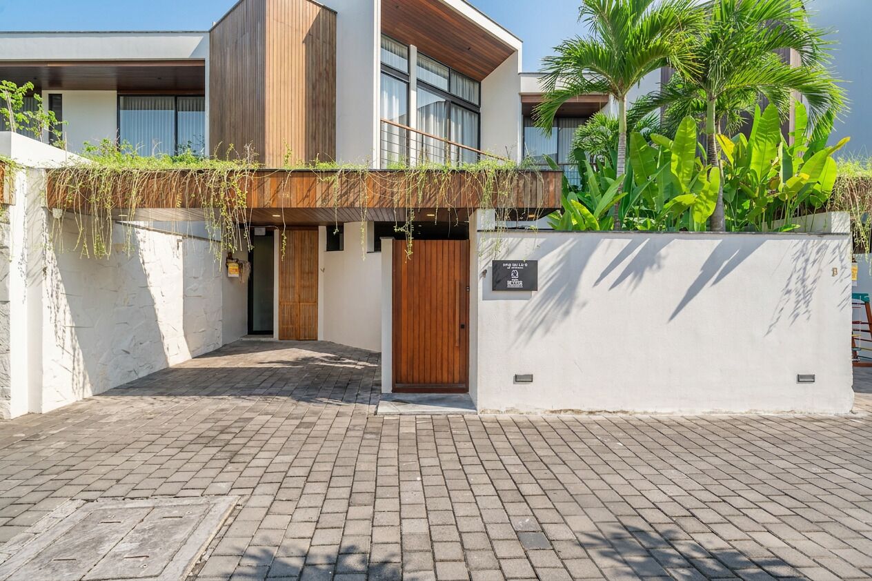 Um edifício moderno com porta de madeira, parede branca com um letreiro e área de entrada pavimentada.