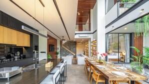 Eine moderne Küche mit Kochinsel, ein Essbereich mit langem Holztisch und eine Treppe, die zu einer oberen Ebene führt.