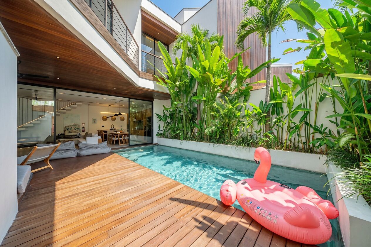 Una casa moderna amb piscina, terrassa de fusta i plantes tropicals.