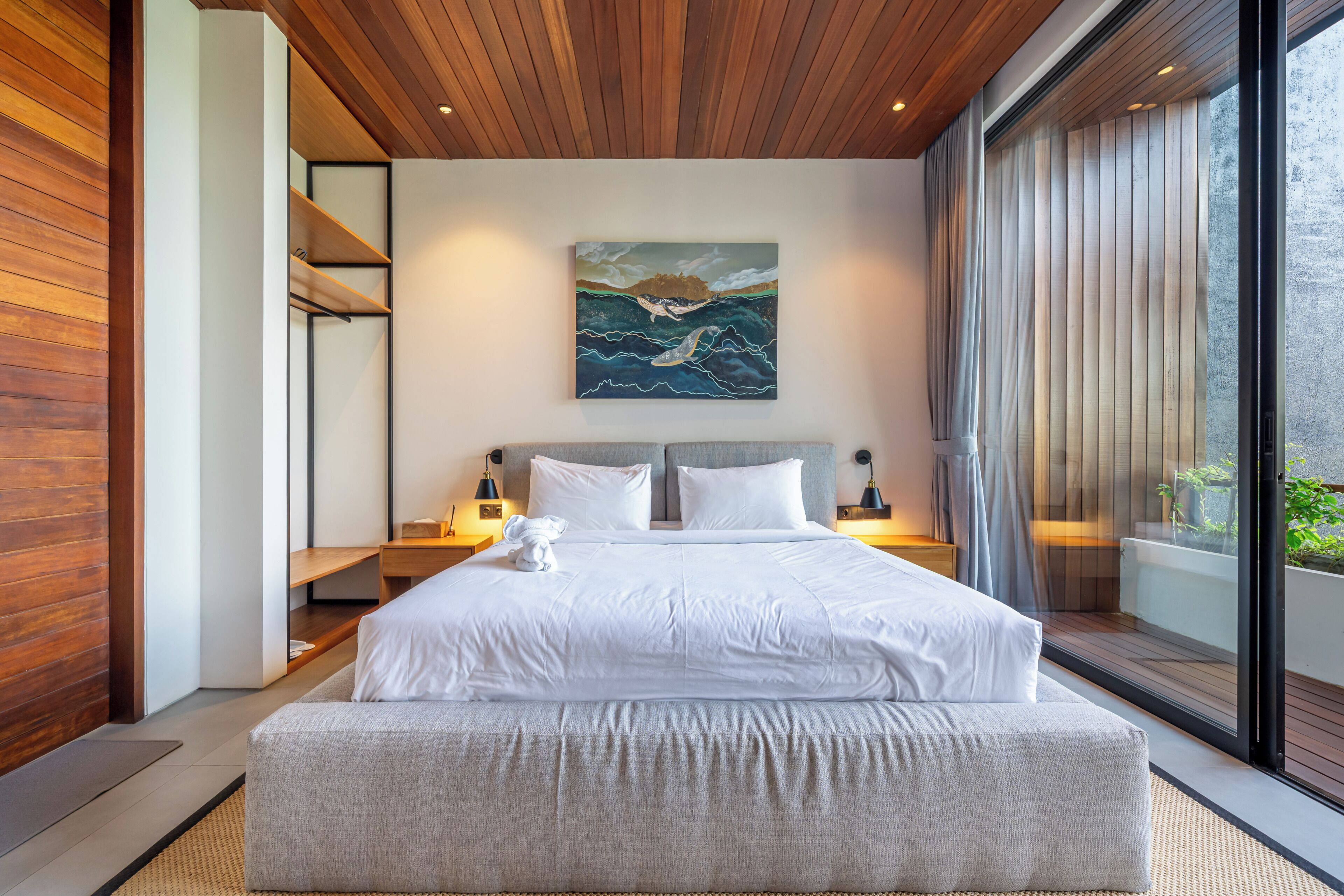 A modern bedroom with a large bed, wooden ceiling, and a painting above the bed.