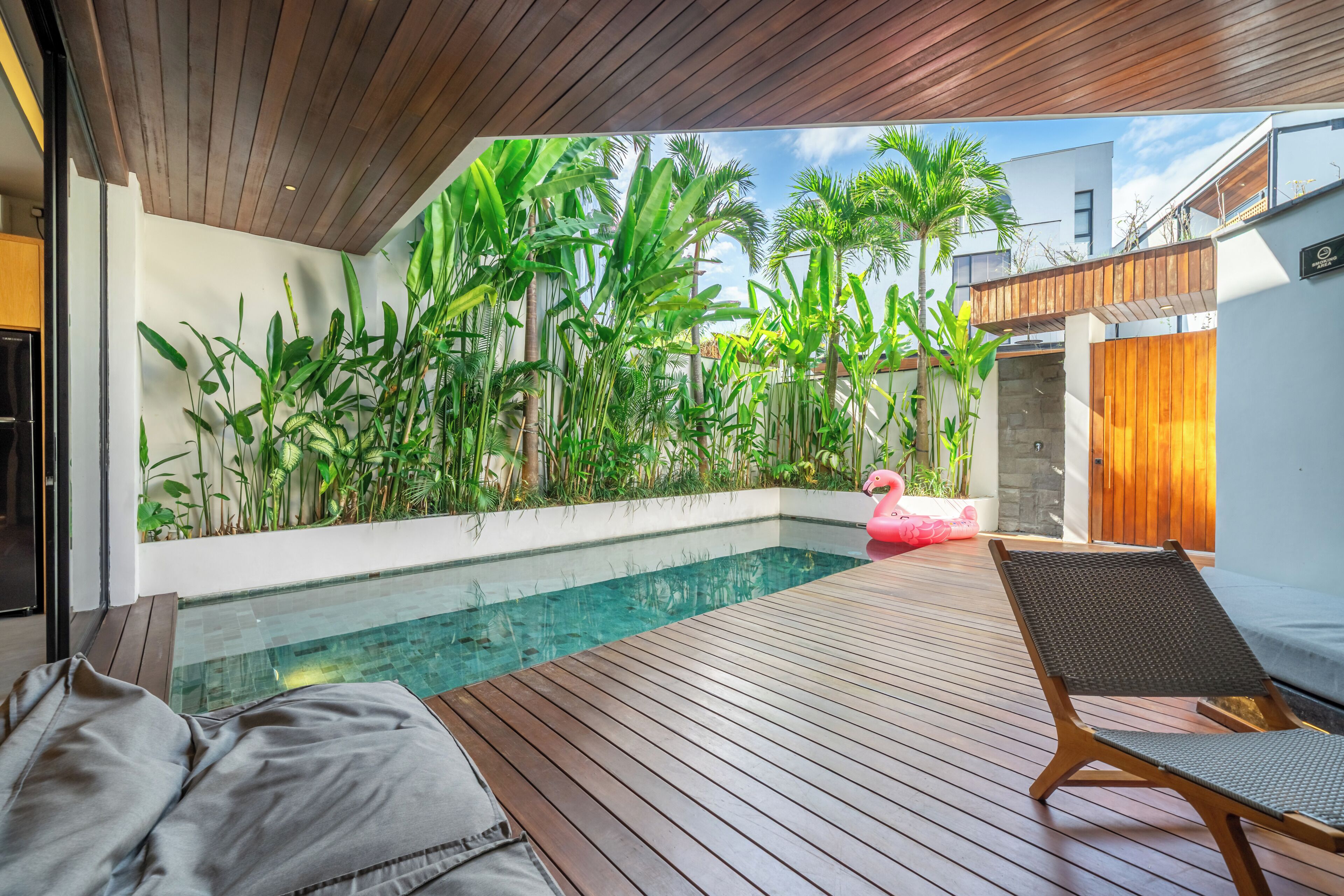 Terraza de madera con piscina, sillas de descanso y plantas tropicales.