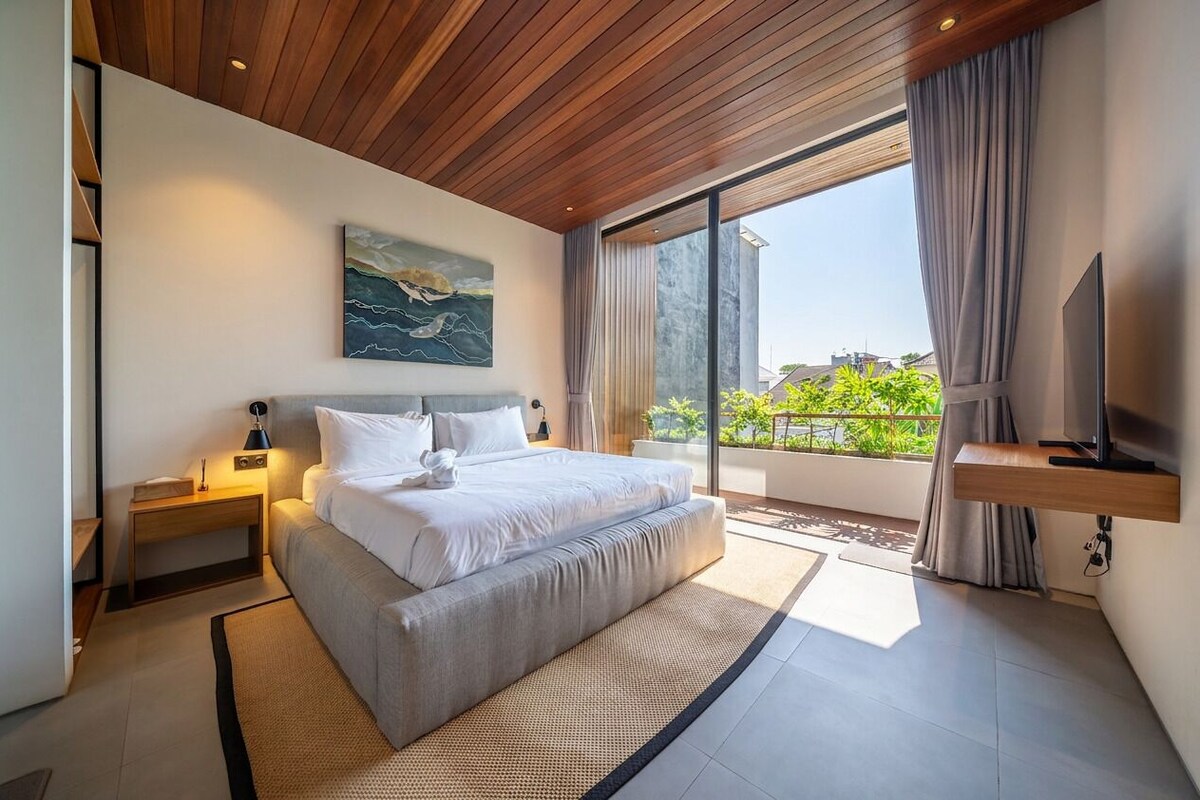 Ein modernes Schlafzimmer mit einem großen Bett, einem Gemälde, einem Fernseher und einem Balkon mit Aussicht.