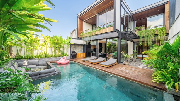 Ein modernes Haus mit Swimmingpool, Liegestühlen und üppiger Bepflanzung.