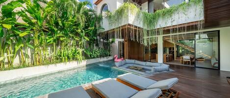 A modern house with a swimming pool, lounge chairs, and lush greenery.
