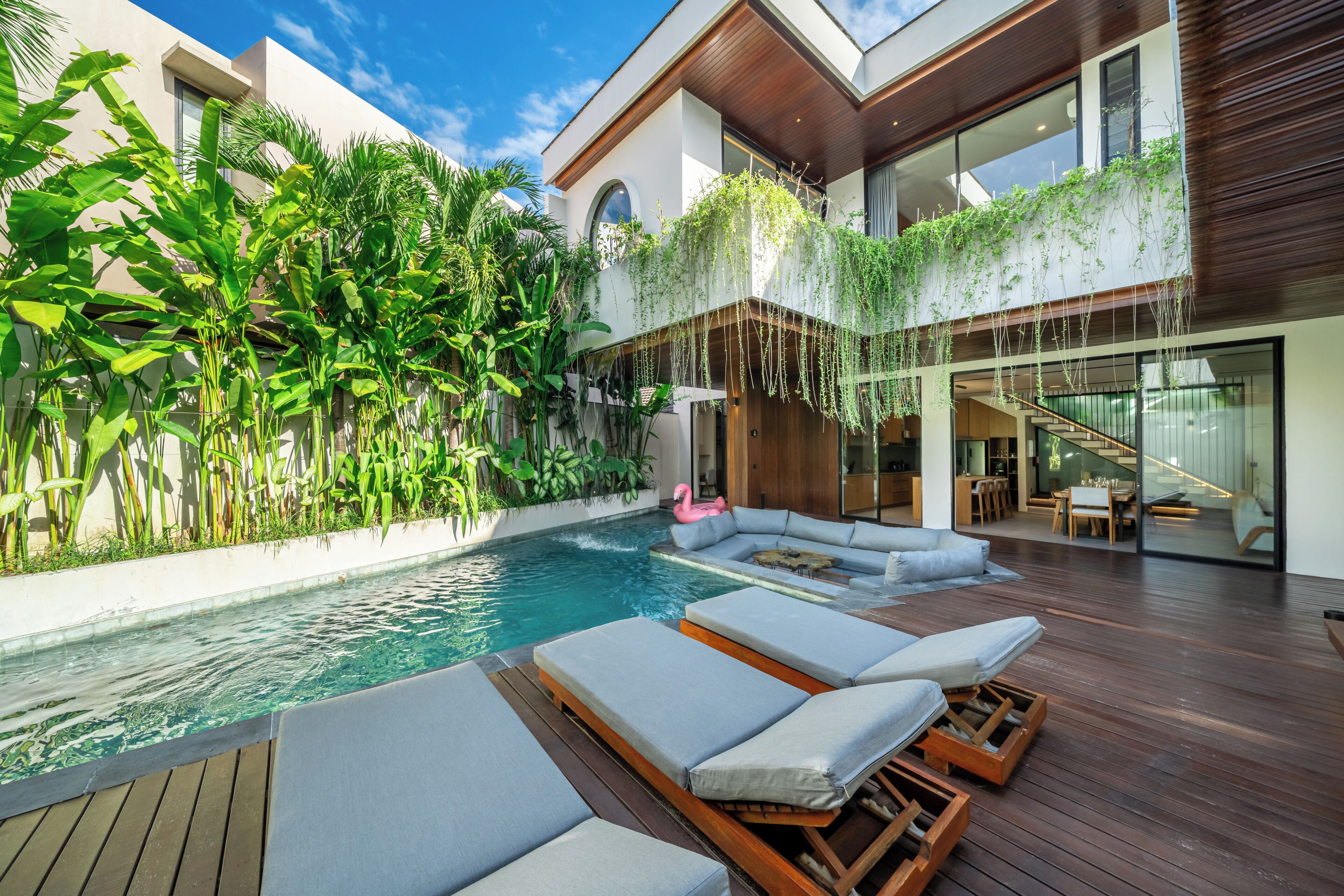 A modern pool area with lounge chairs, a wooden deck, and lush greenery.