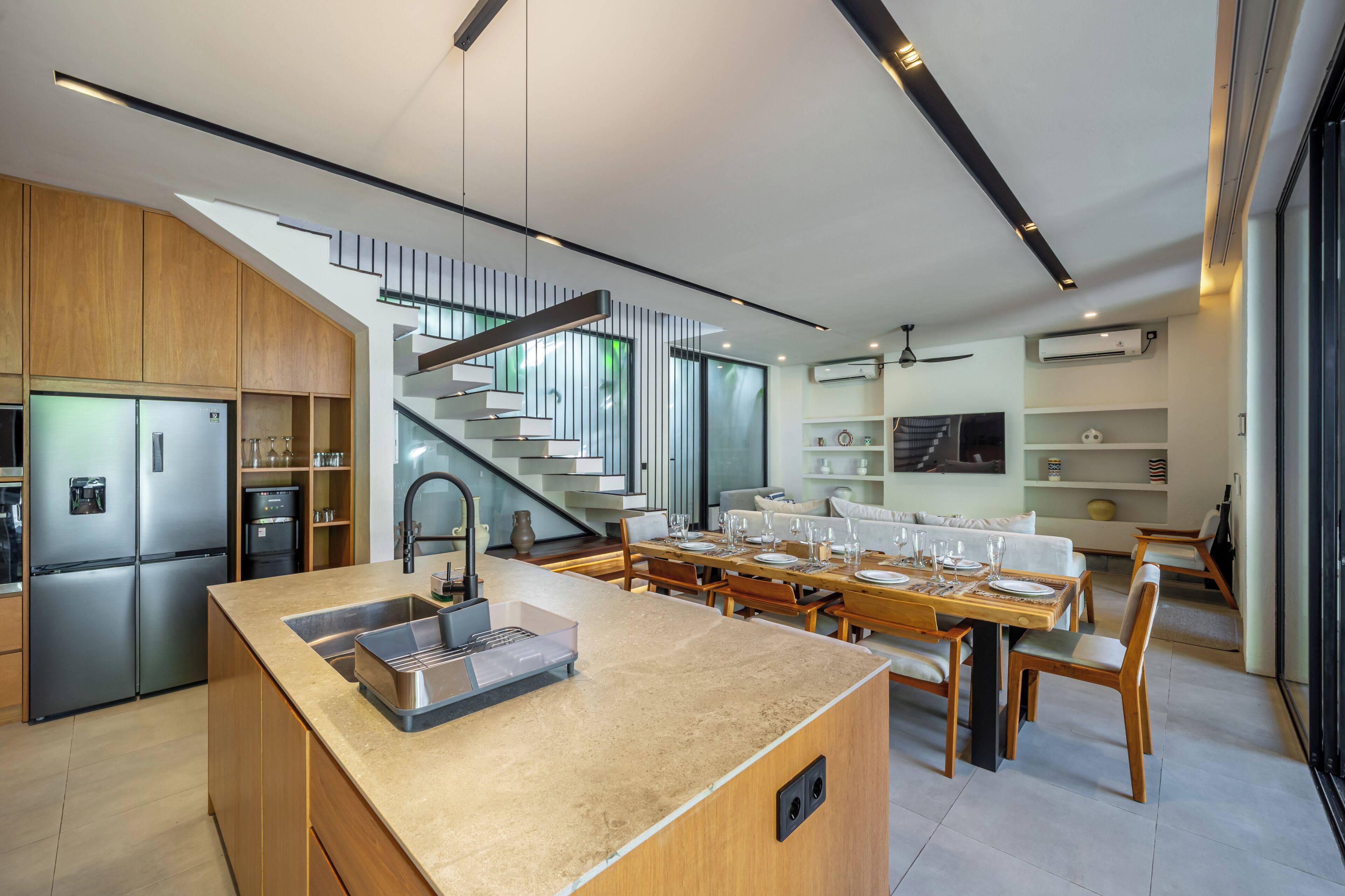 Una cocina moderna con una isla central, electrodomésticos integrados y un comedor con una escalera.