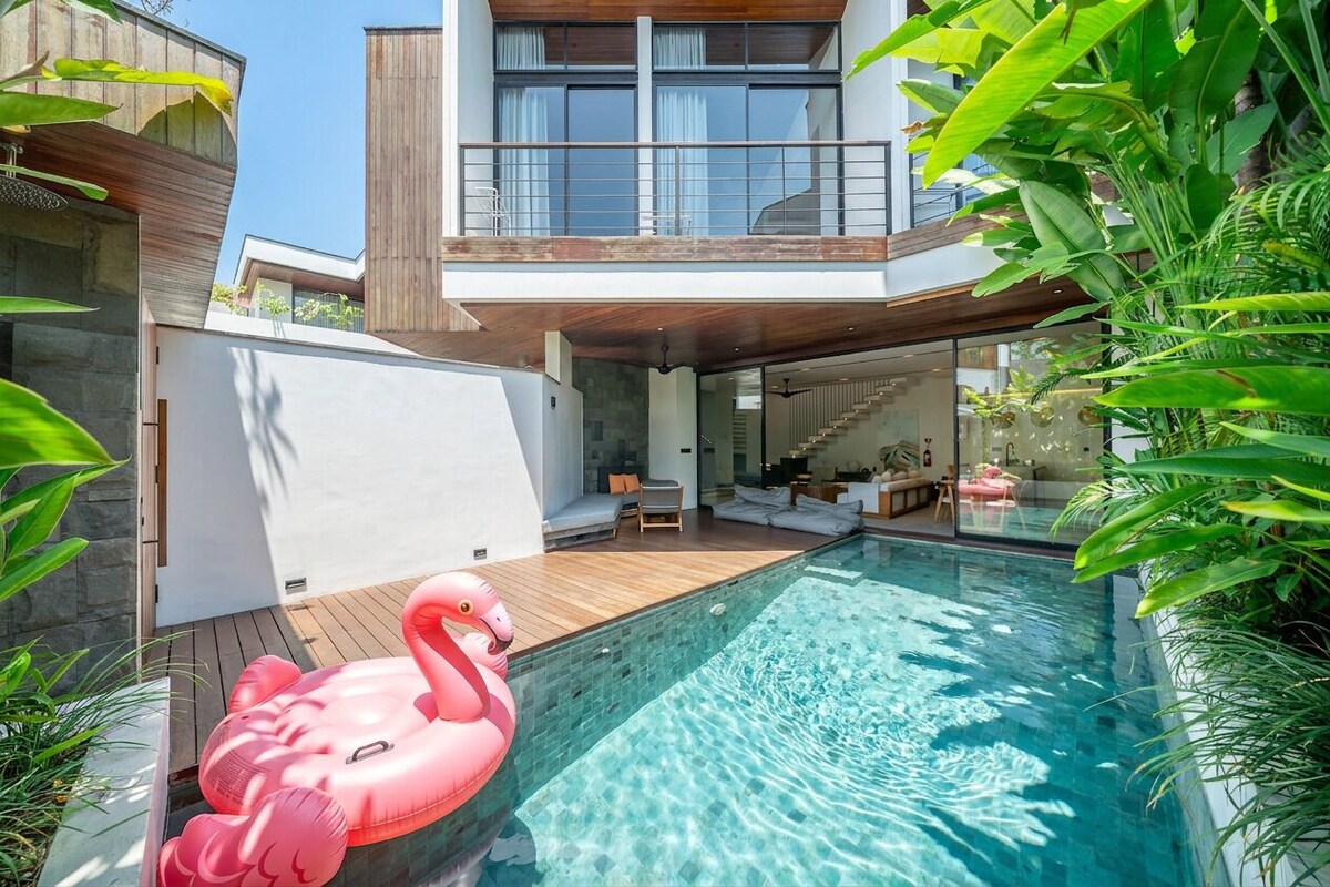 Ein modernes Haus mit Swimmingpool, einem Flamingo-Schwimmpfad und üppigem Grün.