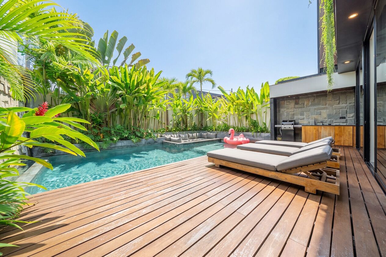 A wooden deck with a pool, lounge chairs, and tropical plants.