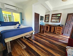 Una stanza con un letto, pavimento in legno, angolo cottura con mobili e una finestra con tende.