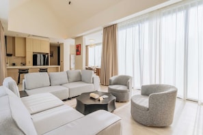 Un salon moderne avec un canapé, des fauteuils, une table basse et un coin cuisine à l’arrière-plan.