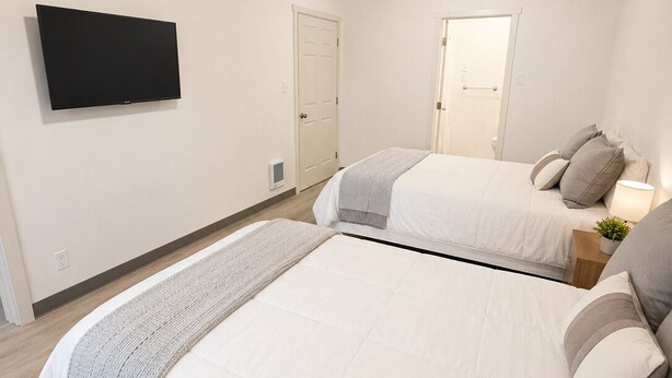 A bedroom with two beds, a TV mounted on the wall, and a door leading to another room.